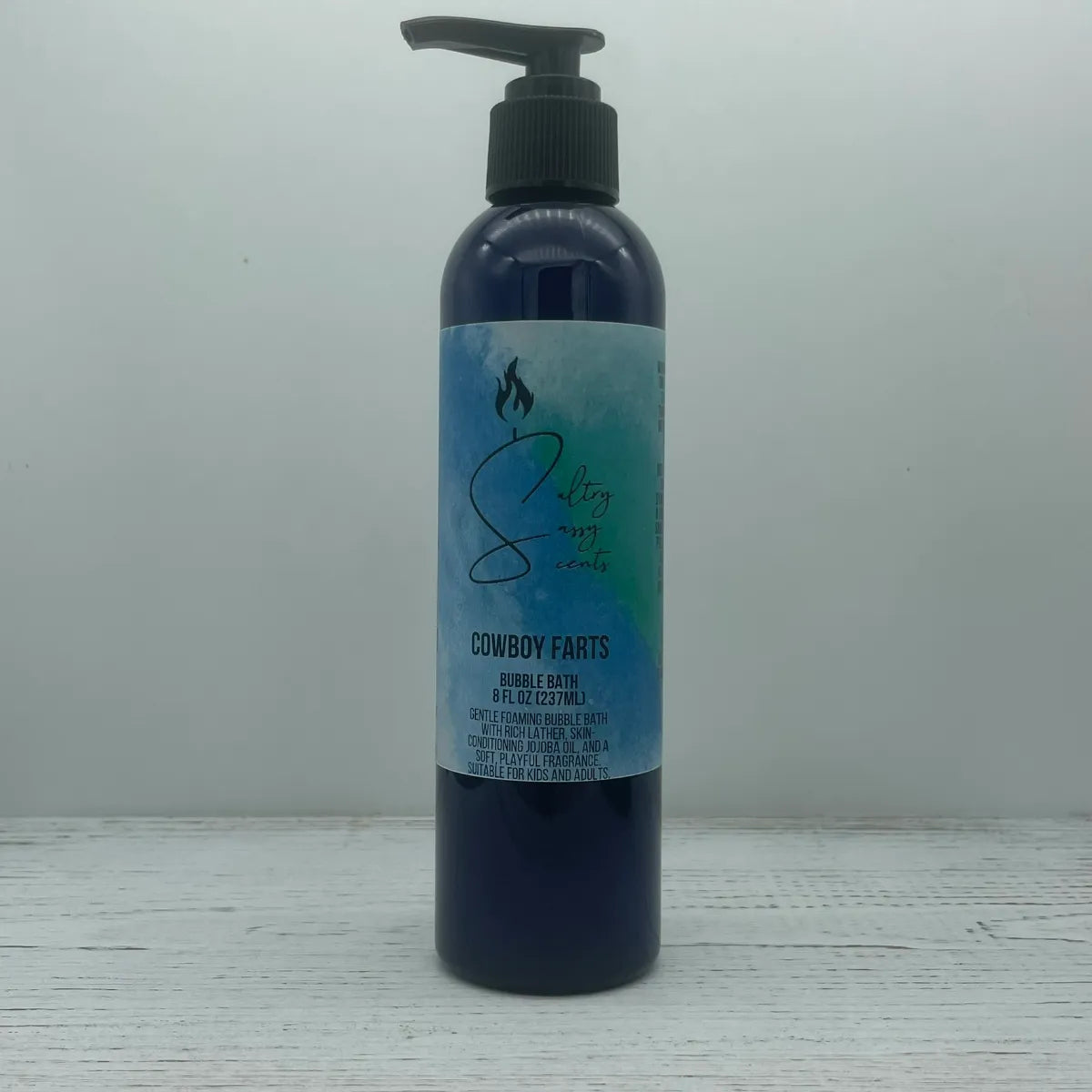 Front label view of a large 8-ounce blue pump bottle containing Sultry Sassy Scents "Cowboy Farts" Bubble Bath, highlighting the gentle foaming formula description.
