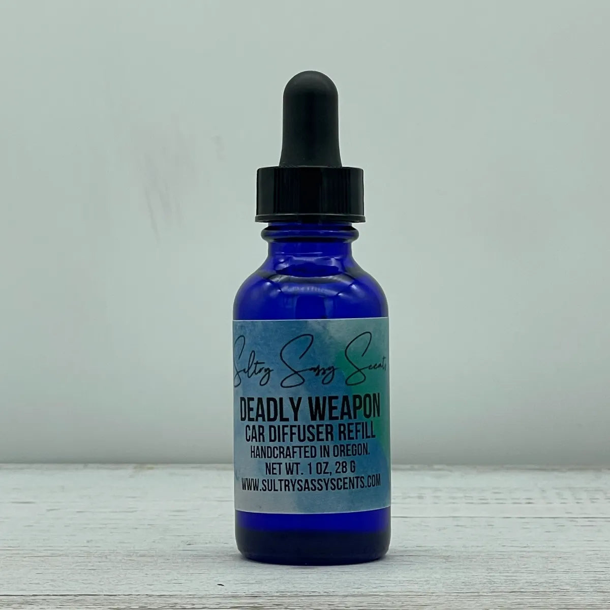 Front label view of a blue glass dropper bottle for Sultry Sassy Scents "Deadly Weapon" Car Diffuser Refill, centered against a crisp light backdrop.