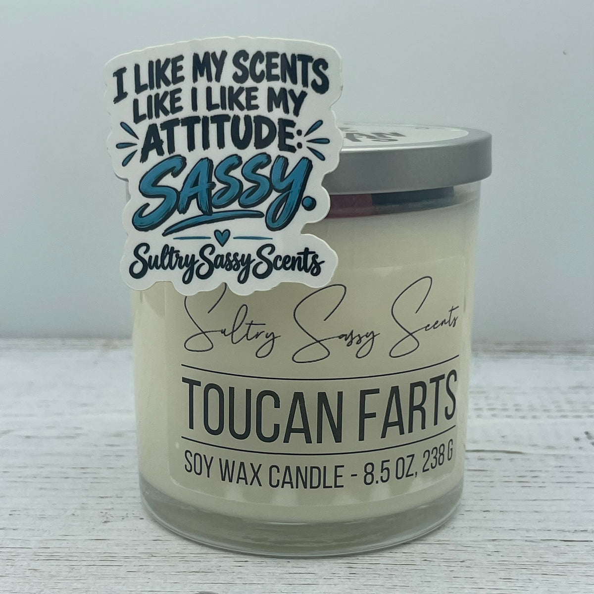Sassy attitude die cut sticker propped against a Toucan Farts soy wax candle