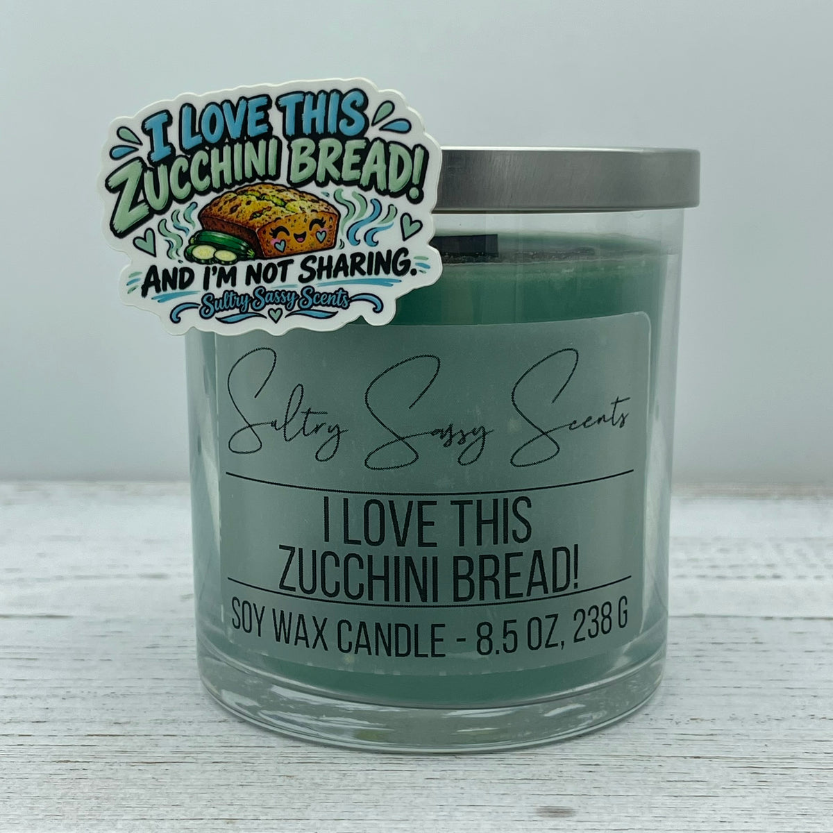 Cozy autumn bakery sticker titled I Love This Zucchini Bread And I'm Not Sharing propped on an 8.5 oz green soy wax candle jar.