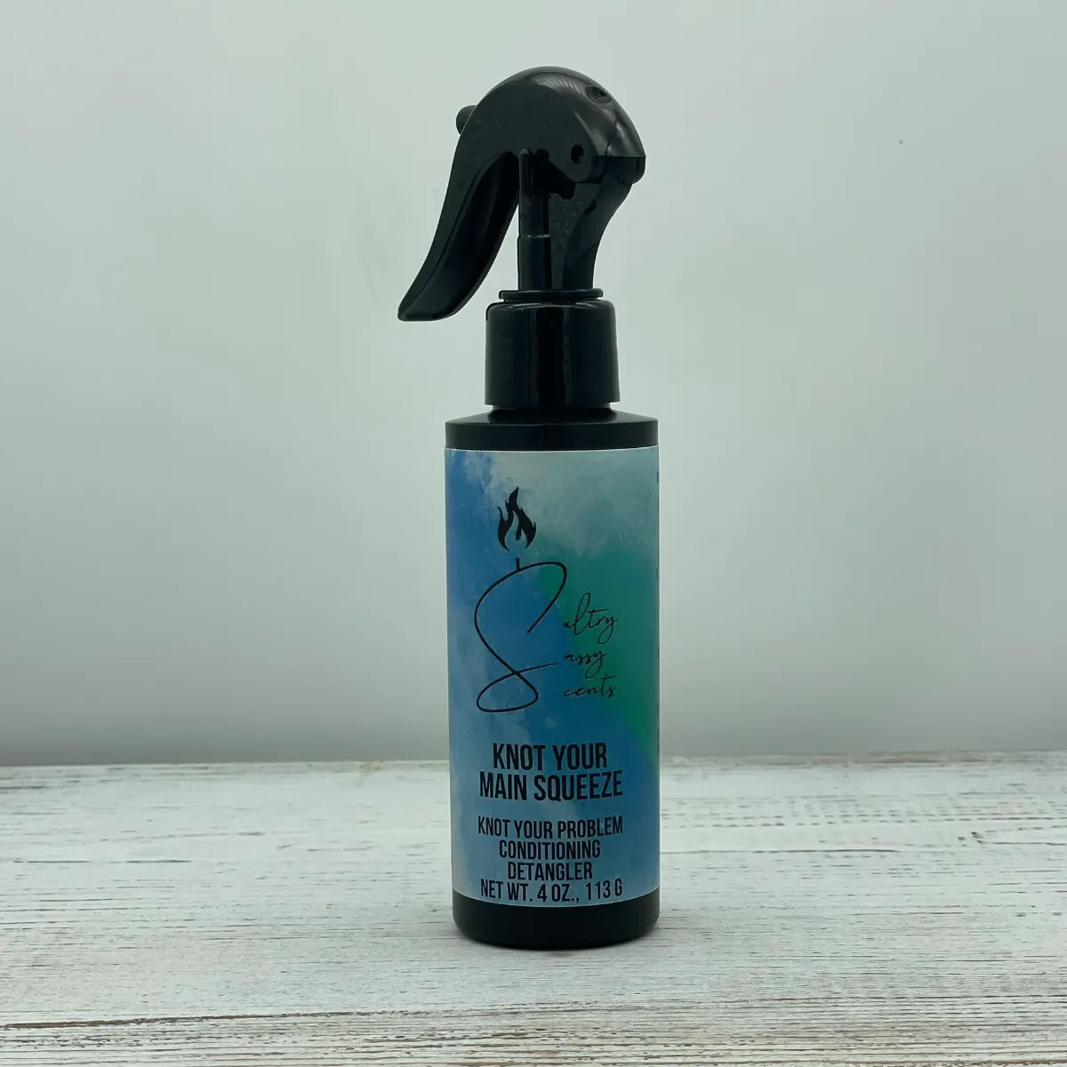 A single black spray bottle of Sultry Sassy Scents Knot Your Problem Conditioning Detangler in the Knot Your Main Squeeze variation, centered on a light wood background.