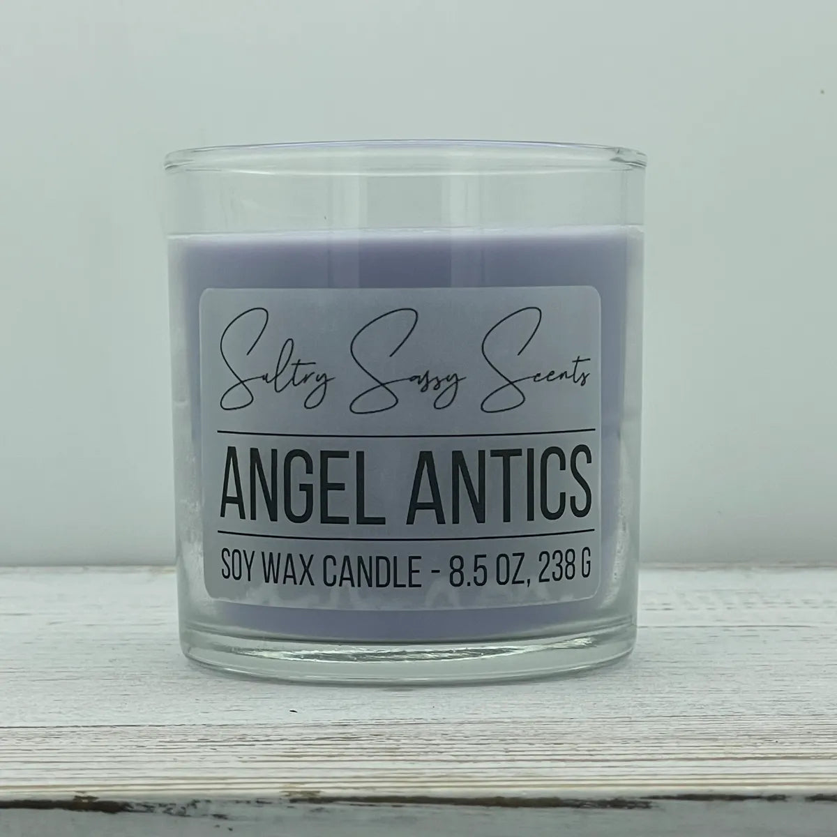 An 8.5-ounce jar of Sultry Sassy Scents "Angel Antics" soy wax candle featuring a soft purple wax color, displayed against a clean light background.