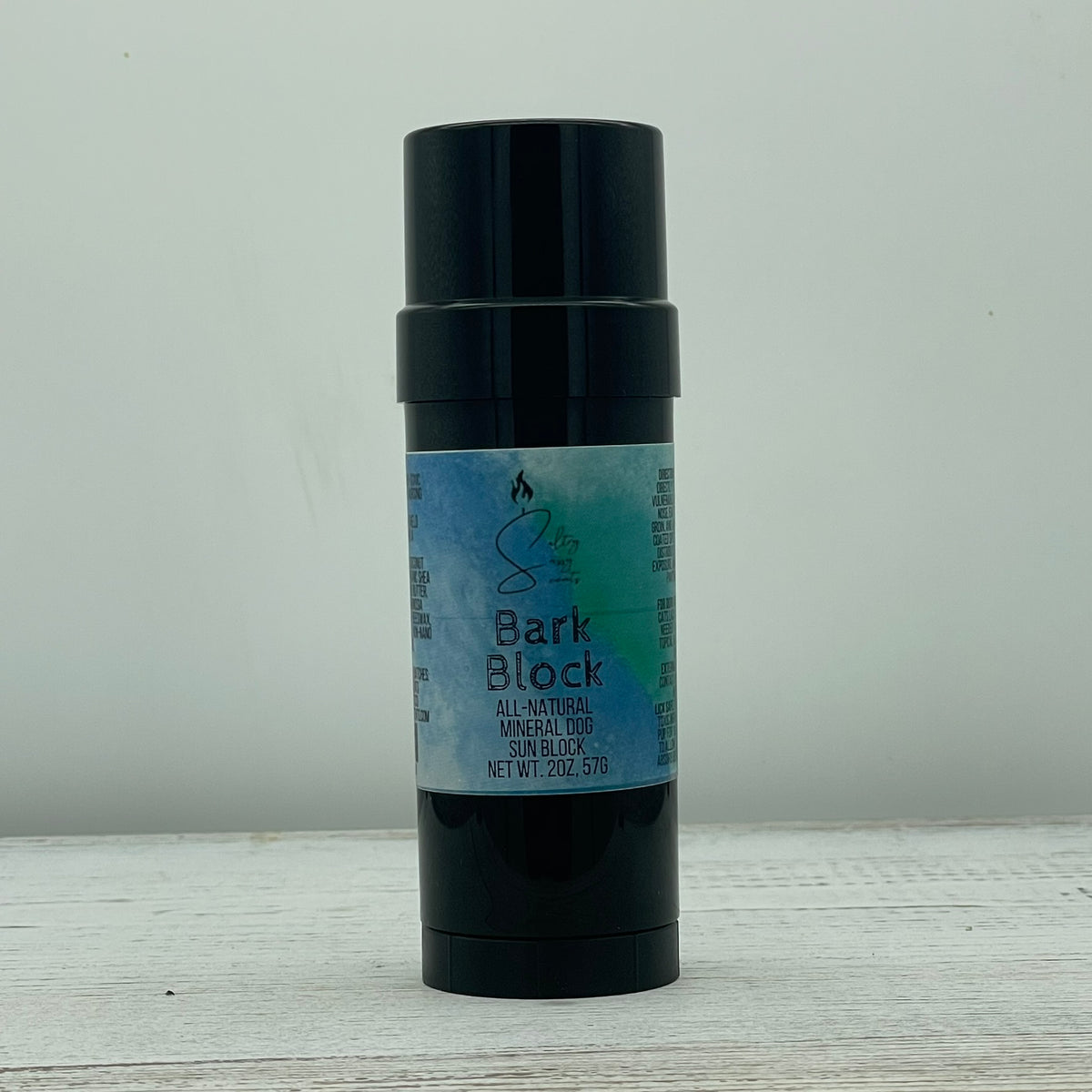 Front view of a closed 2-ounce black twist-up stick container of Sultry Sassy Scents Bark Block All-Natural Mineral Dog Sun Block, featuring the signature blue and green watercolor branding label.