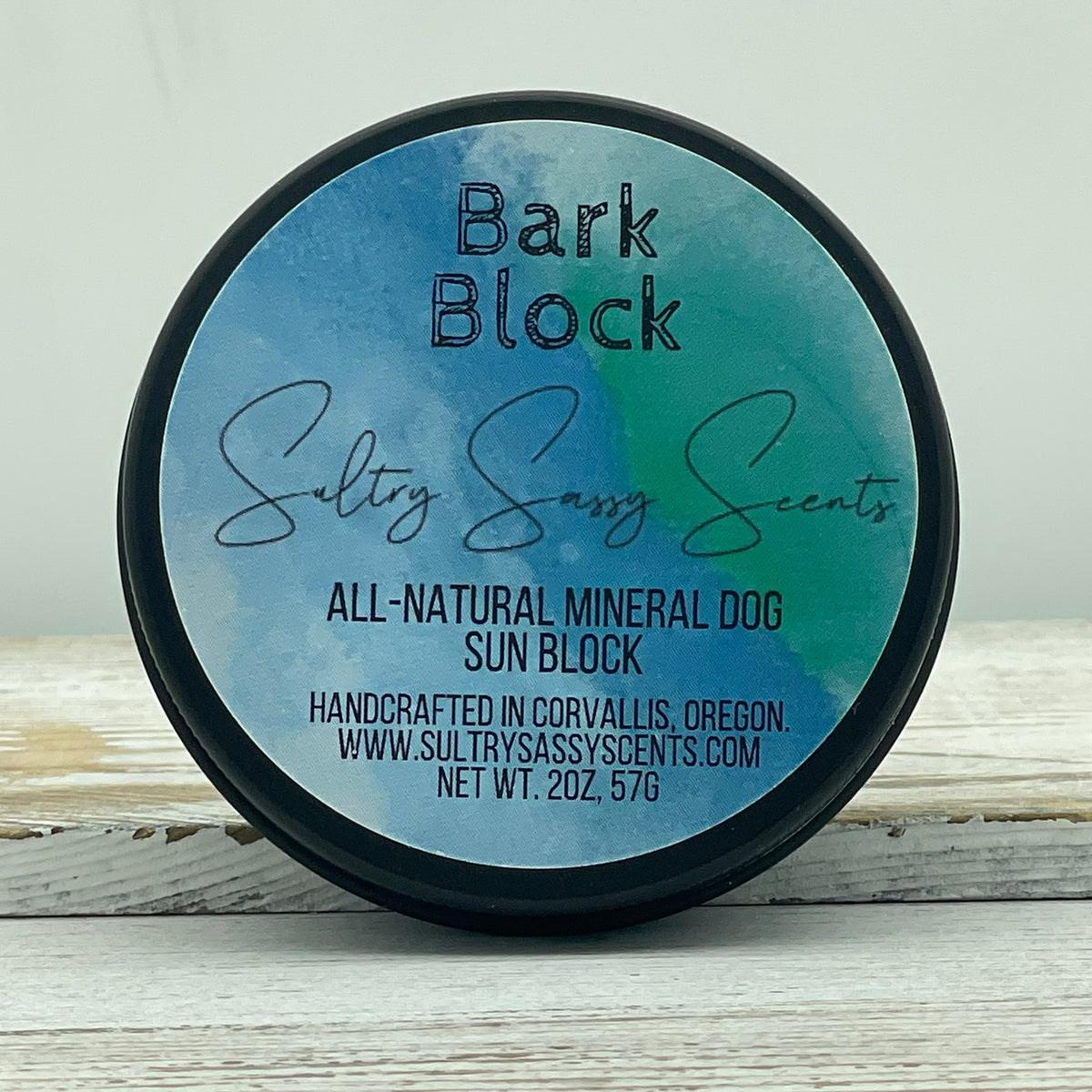Top view of a closed 2-ounce round black tin for Sultry Sassy Scents Bark Block All-Natural Mineral Dog Sun Block, highlighting the text showing it is handcrafted in Corvallis, Oregon.