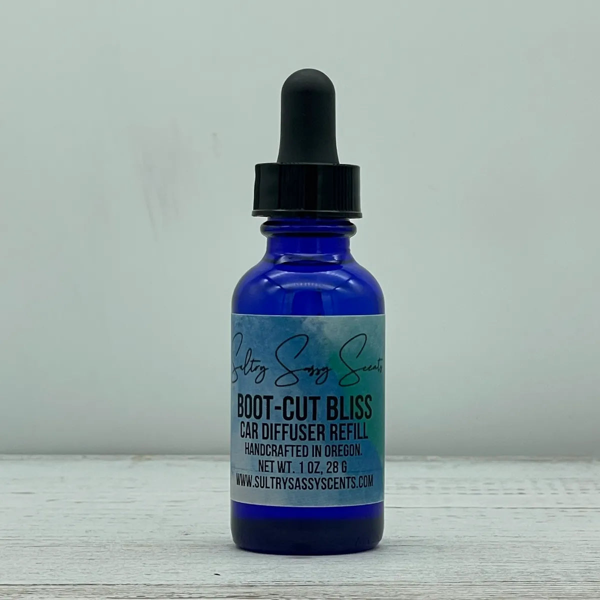 Front label view of a blue glass dropper bottle for Sultry Sassy Scents "Boot-Cut Bliss" Car Diffuser Refill, highlighting the brand logo and 1 ounce sizing text.