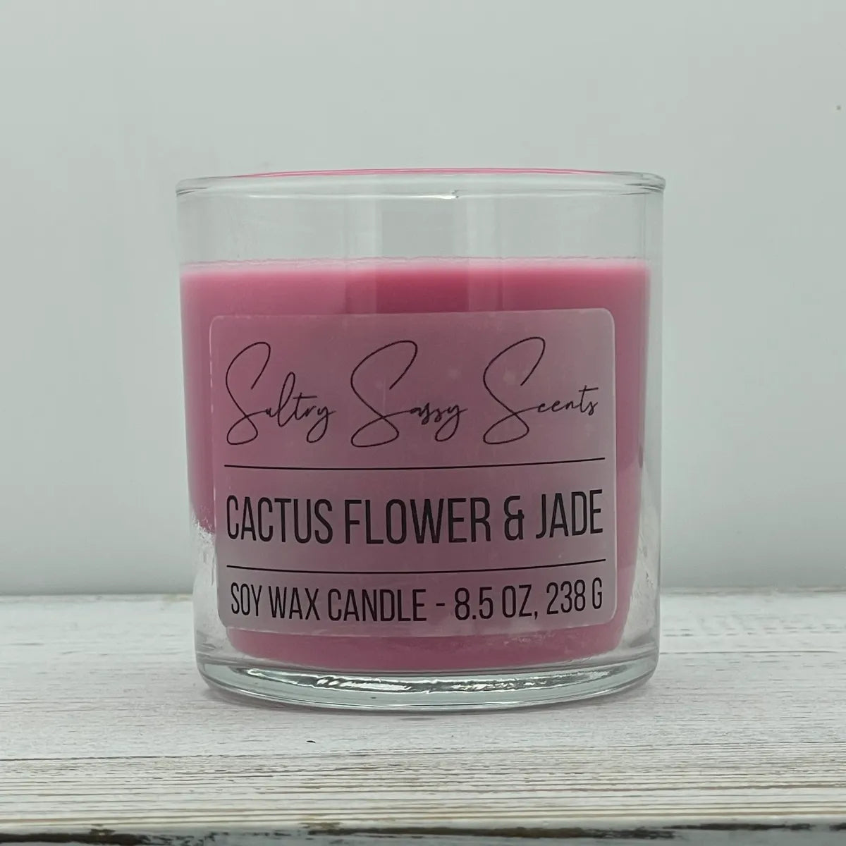 An 8.5-ounce clear glass jar of Sultry Sassy Scents "Cactus Flower & Jade" soy wax candle featuring a rich, solid dark pink wax color, centered on a light wood surface.