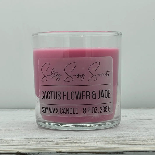 An 8.5-ounce clear glass jar of Sultry Sassy Scents "Cactus Flower & Jade" soy wax candle featuring a rich, solid dark pink wax color, centered on a light wood surface.
