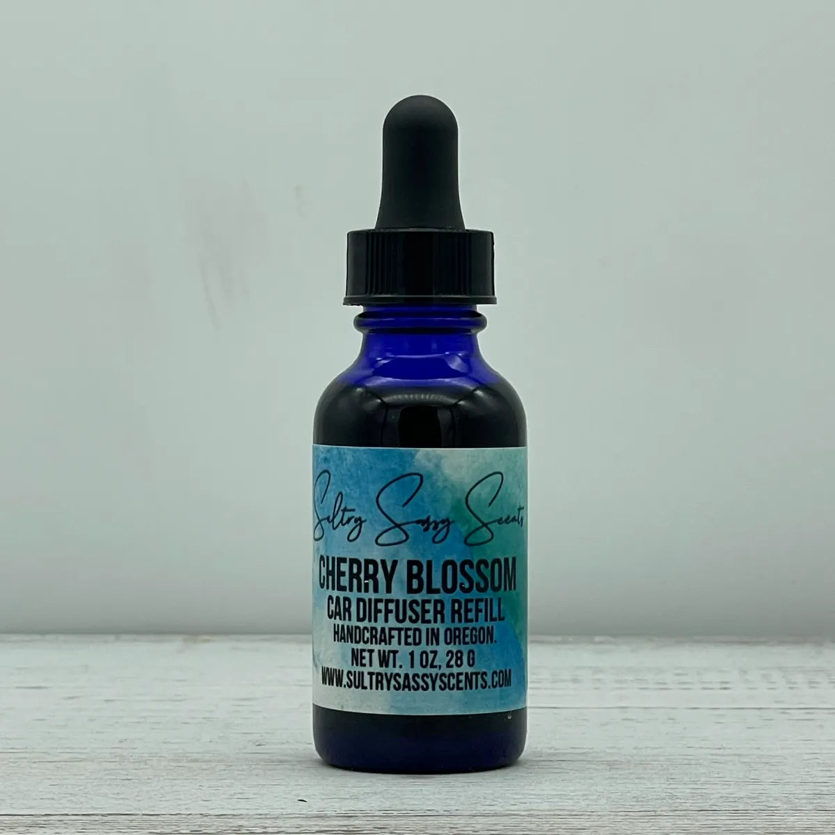Front label view of a blue glass dropper bottle for Sultry Sassy Scents "Cherry Blossom" Car Diffuser Refill, featuring the signature watercolor label background.