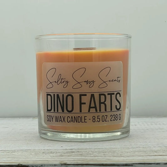 An 8.5-ounce clear glass jar of Sultry Sassy Scents "Dino Farts" soy wax candle showcasing a warm terracotta orange wax color and a flat wooden wick.