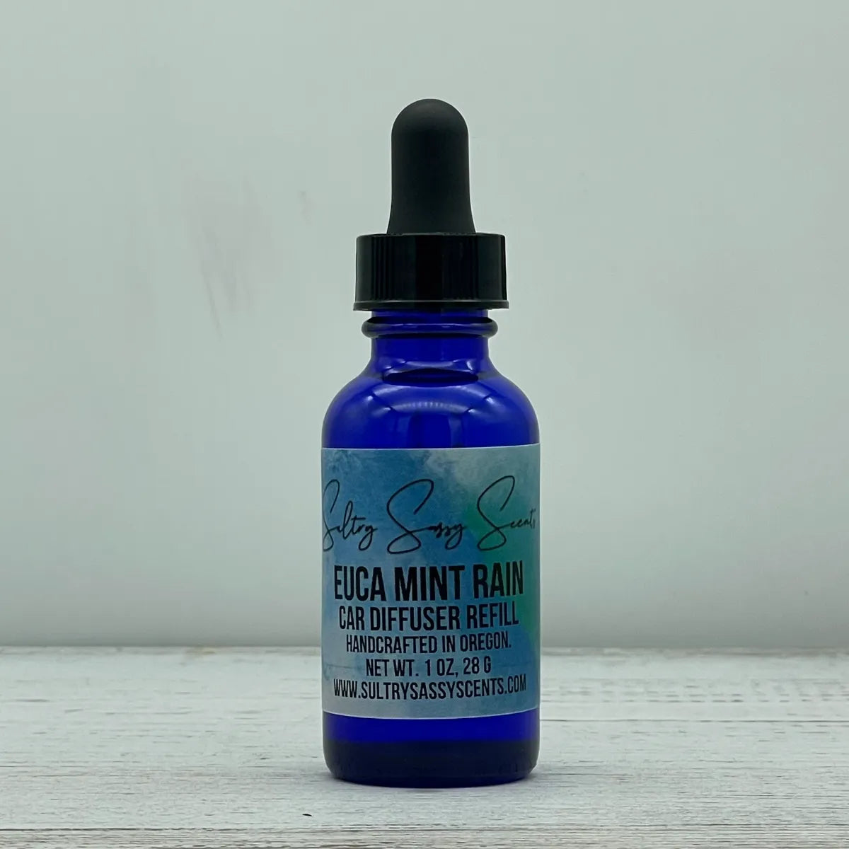 Front label view of a blue glass dropper bottle for Sultry Sassy Scents "Euca Mint Rain" Car Diffuser Refill, displaying the official brand website text.
