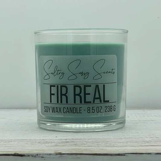 An 8.5-ounce clear glass jar of Sultry Sassy Scents "Fir Real" soy wax candle showcasing a deep muted pine green wax color with a flat wooden wick, positioned against a clean light background.