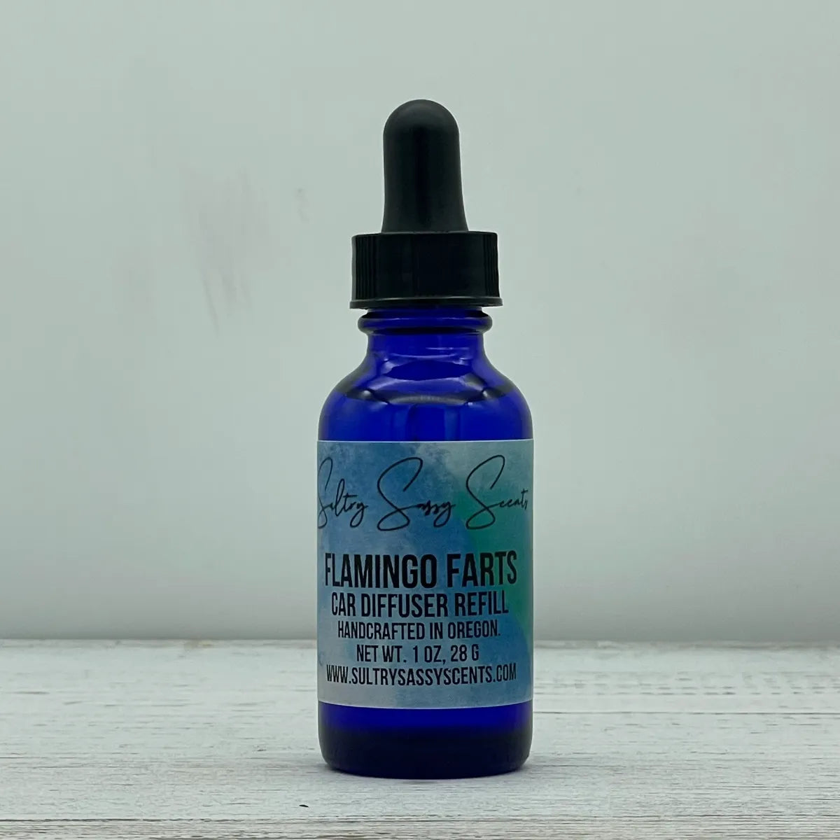 Front label view of a blue glass dropper bottle for Sultry Sassy Scents "Flamingo Farts" Car Diffuser Refill, showcasing the playful scent name over a blue-toned label.