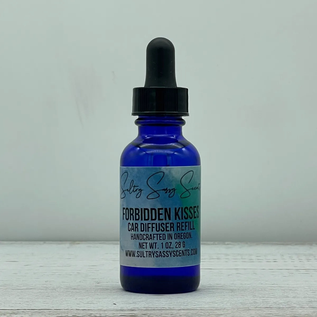 Front label view of a blue glass dropper bottle for Sultry Sassy Scents "Forbidden Kisses" Car Diffuser Refill, detailing the handcrafted product line info.