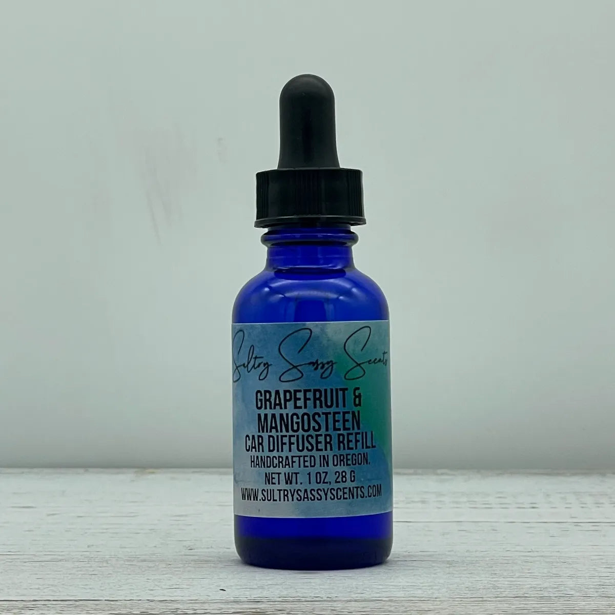 Front label view of a cobalt blue glass dropper bottle containing Sultry Sassy Scents "Grapefruit & Mangosteen" Car Diffuser Refill, detailing the 1 ounce net weight.