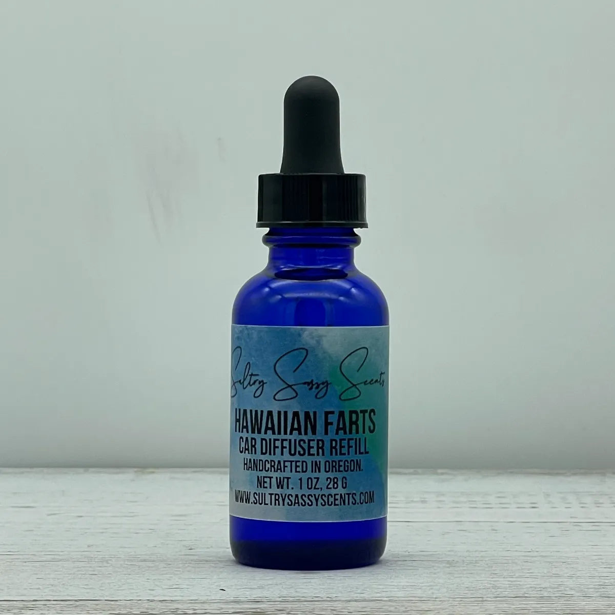 Front label view of a cobalt blue glass dropper bottle containing Sultry Sassy Scents "Hawaiian Farts" Car Diffuser Refill, displaying the official brand logo script and typography design.