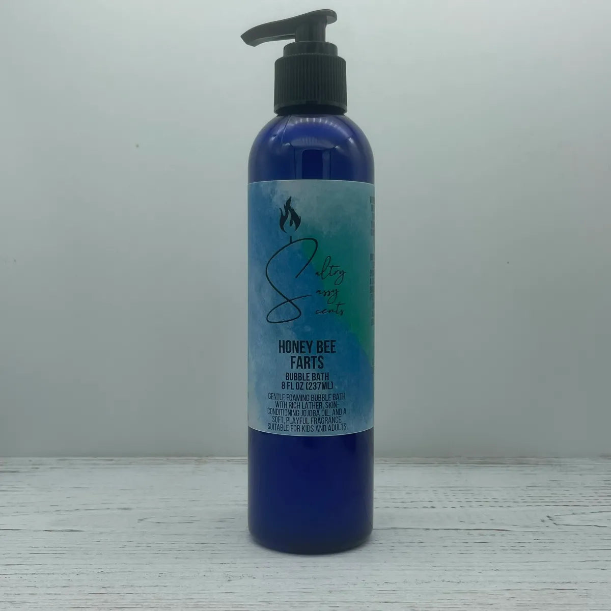 Front label view of a large 8-ounce blue pump bottle containing Sultry Sassy Scents "Honey Bee Farts" Bubble Bath, showcasing the central brand logo design.