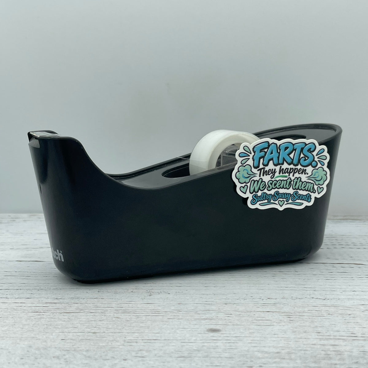Farts They Happen We Scent Them comedic die-cut sticker attached to a office tape dispenser for physical product dimension scale reference.