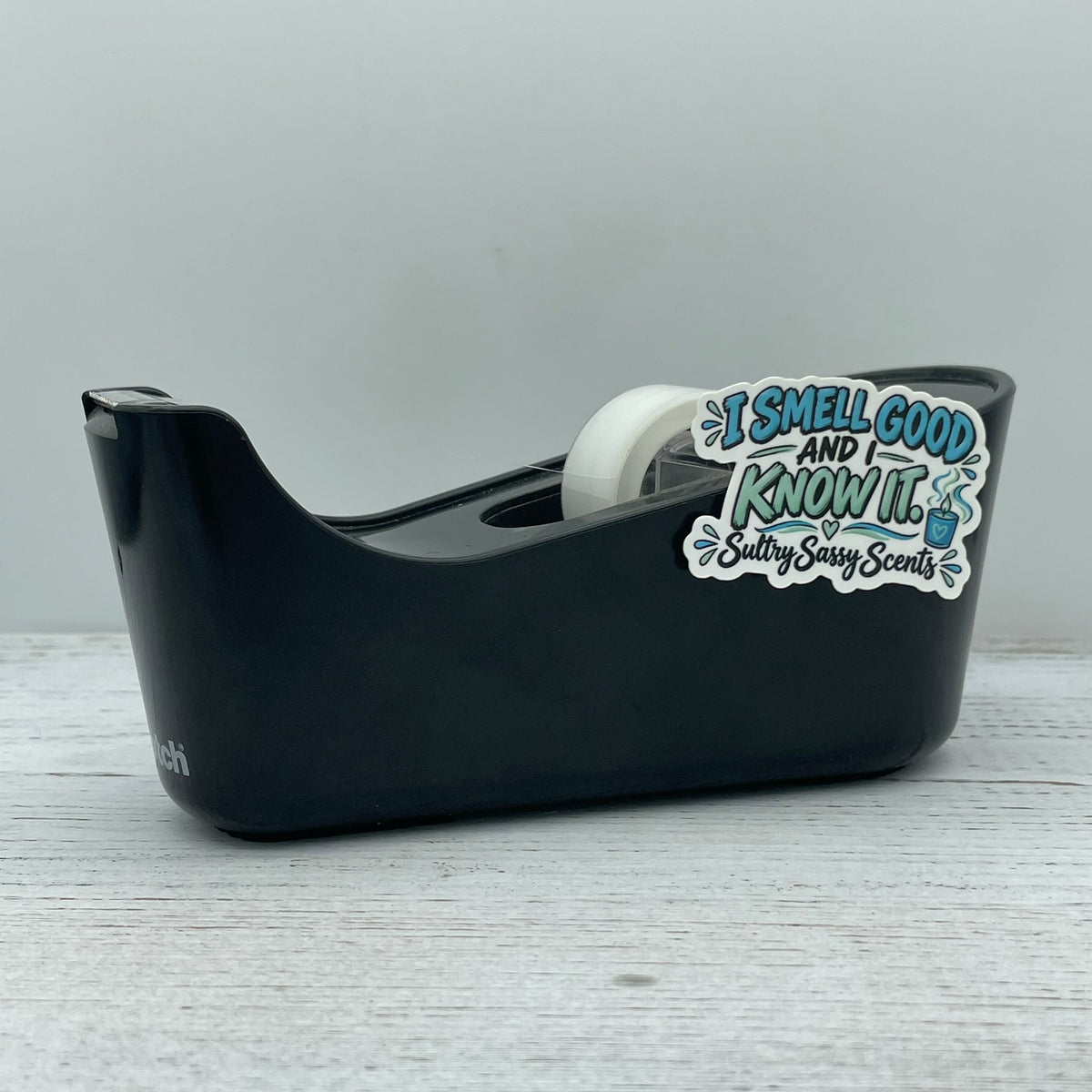I Smell Good and I Know It die-cut vinyl sticker applied to a black desk tape dispenser to show size scaling and daily lifestyle use.