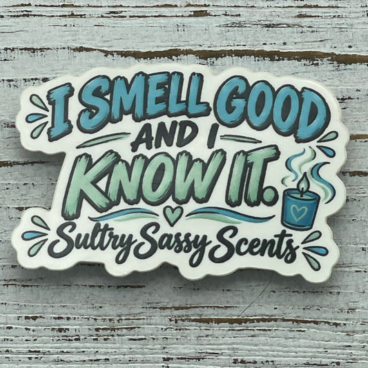 Close-up flat-lay of I Smell Good and I Know It waterproof sticker featuring teal lettering, decorative splashes, and an illustrated burning candle.