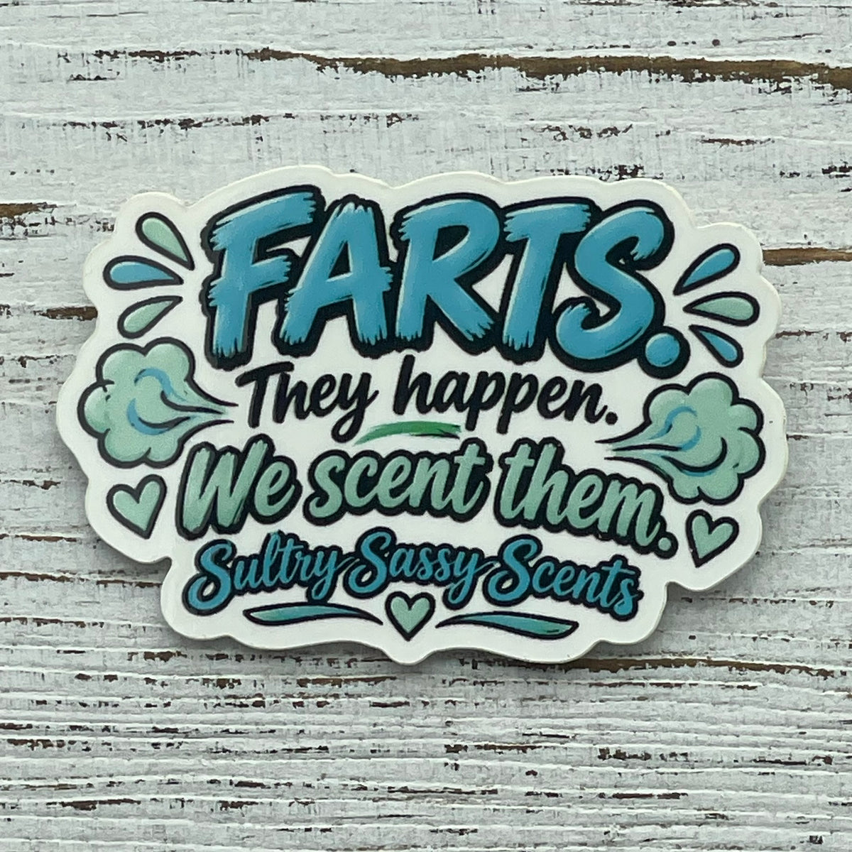 A high-contrast flat-lay photo of Farts They Happen We Scent Them glossy vinyl sticker showing the custom contour shape, teal text, and cloud details.