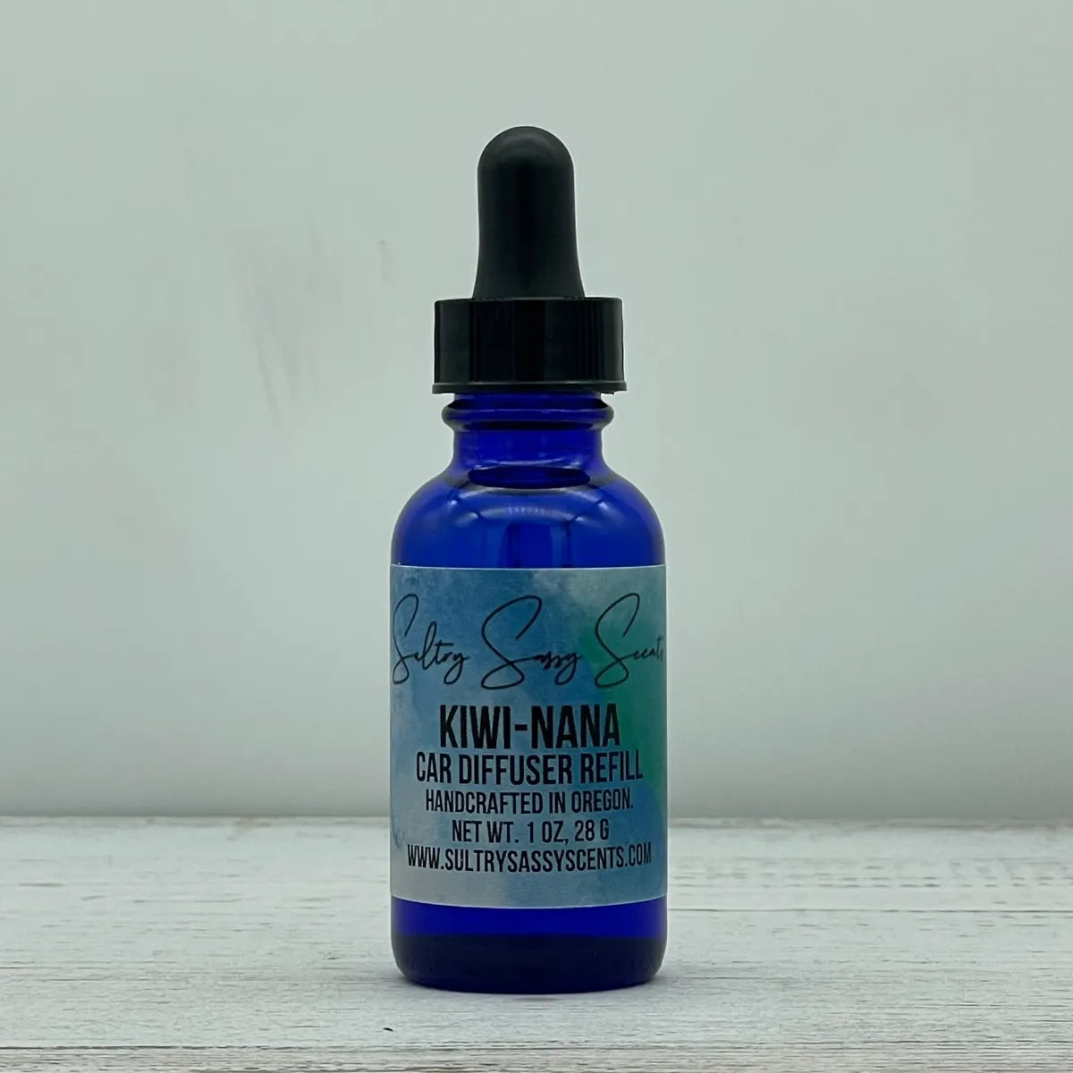 Front label view of a cobalt blue glass dropper bottle containing Sultry Sassy Scents "Kiwi-Nana" Car Diffuser Refill, showcasing the clean blue-toned product label layout.