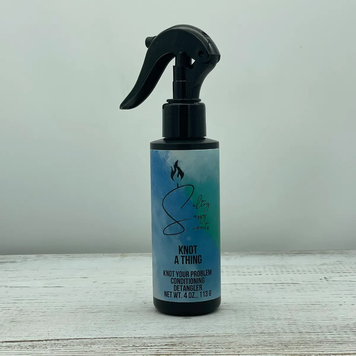 A single black spray bottle of Sultry Sassy Scents Knot Your Problem Conditioning Detangler in the Knot a Thing variation, centered on a light wood background.