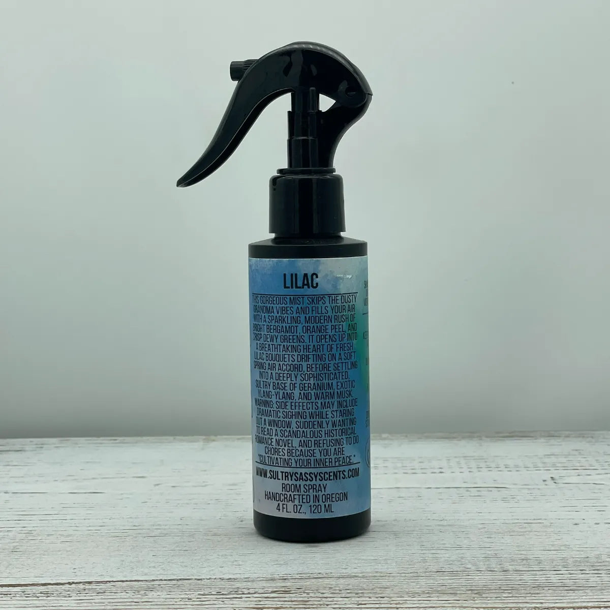 Front label of a black spray bottle for Sultry Sassy Scents "Lilac" Room Spray, displaying a clean layout with text describing a fresh, sophisticated floral bouquet.