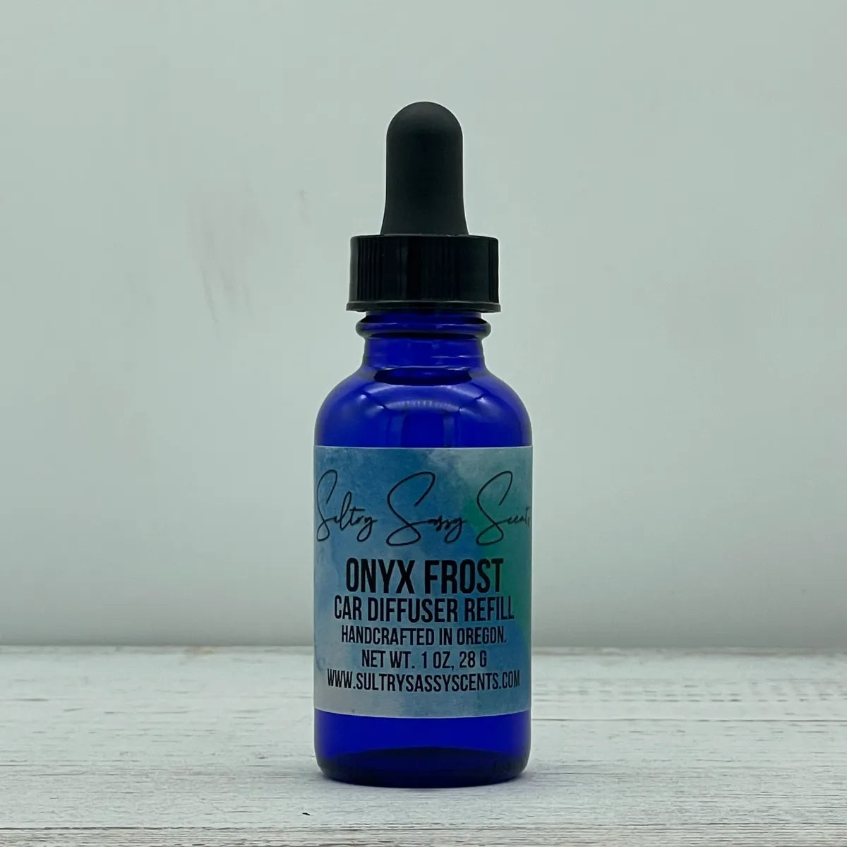Front label view of a cobalt blue glass dropper bottle containing Sultry Sassy Scents "Onyx Frost" Car Diffuser Refill, featuring the signature blue watercolor background design on the label.