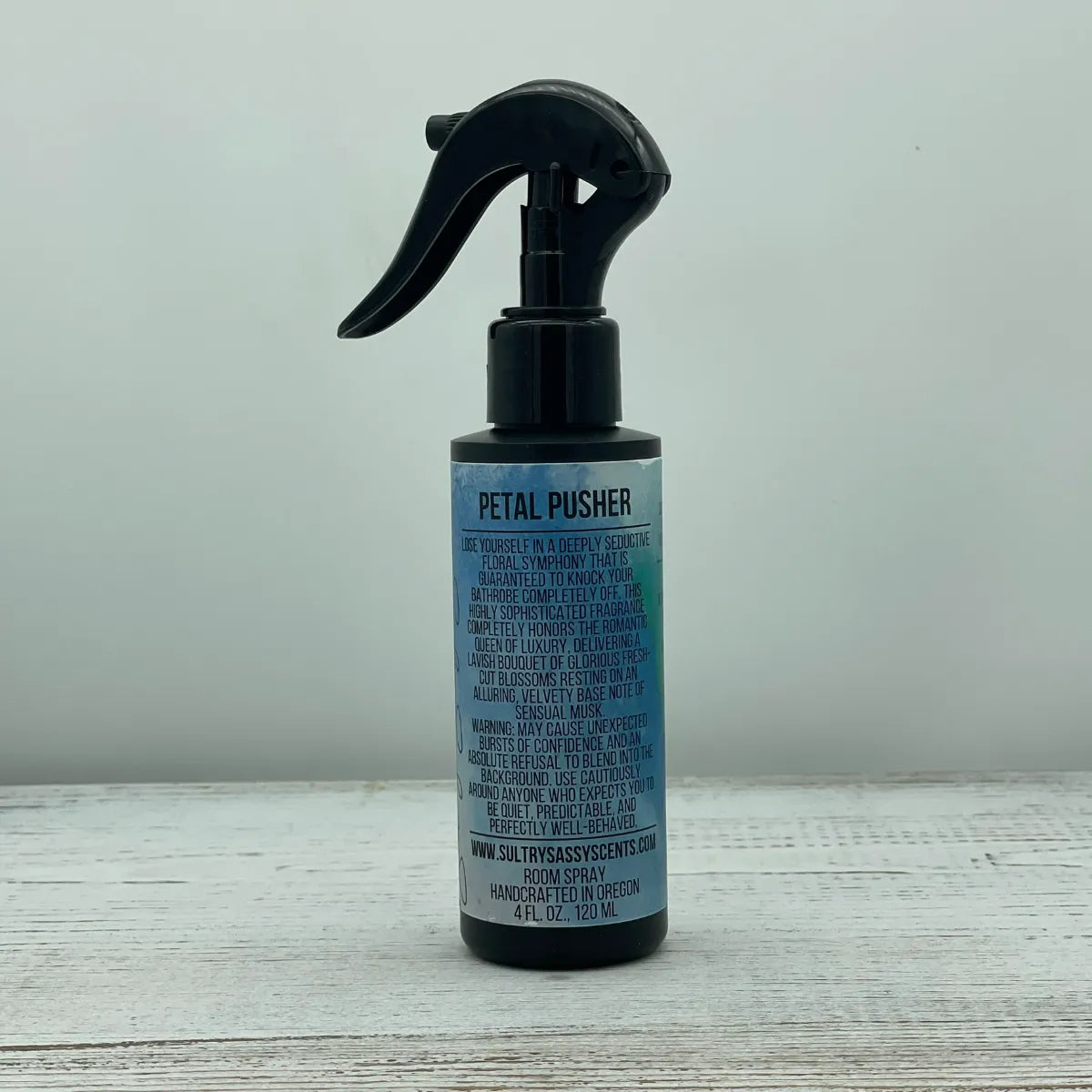 Front label of a black spray bottle for Sultry Sassy Scents "Petal Pusher" Room Spray, featuring stylized text describing a seductive floral symphony fragrance.