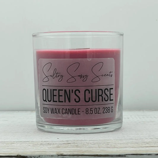 An 8.5-ounce clear glass jar of Sultry Sassy Scents "Queen's Curse" soy wax candle featuring a deep mauve pink wax color, centered against a light gray background.
