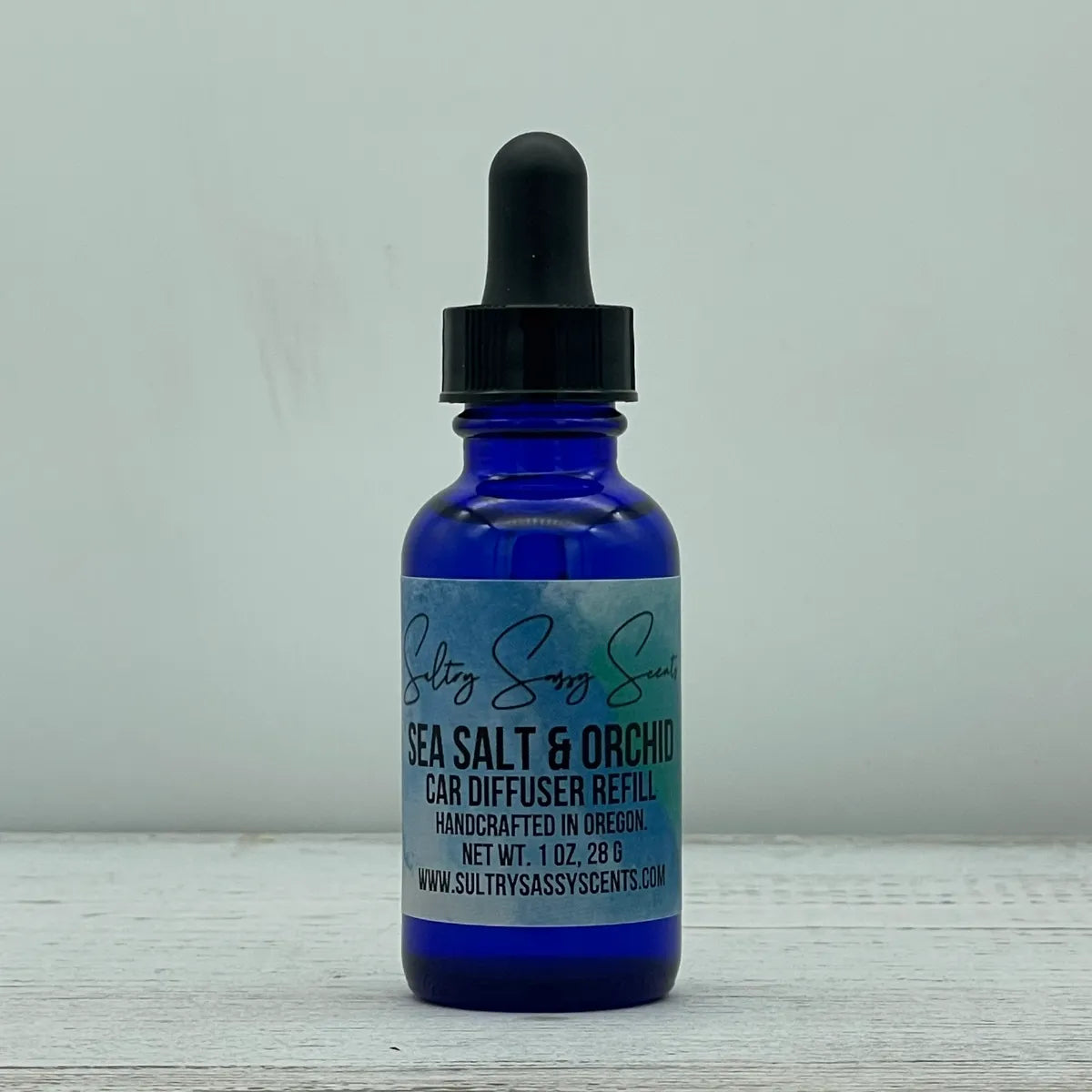 Front label view of a cobalt blue glass dropper bottle containing Sultry Sassy Scents "Sea Salt & Orchid" Car Diffuser Refill, showcasing the clean blue-toned product label layout.
