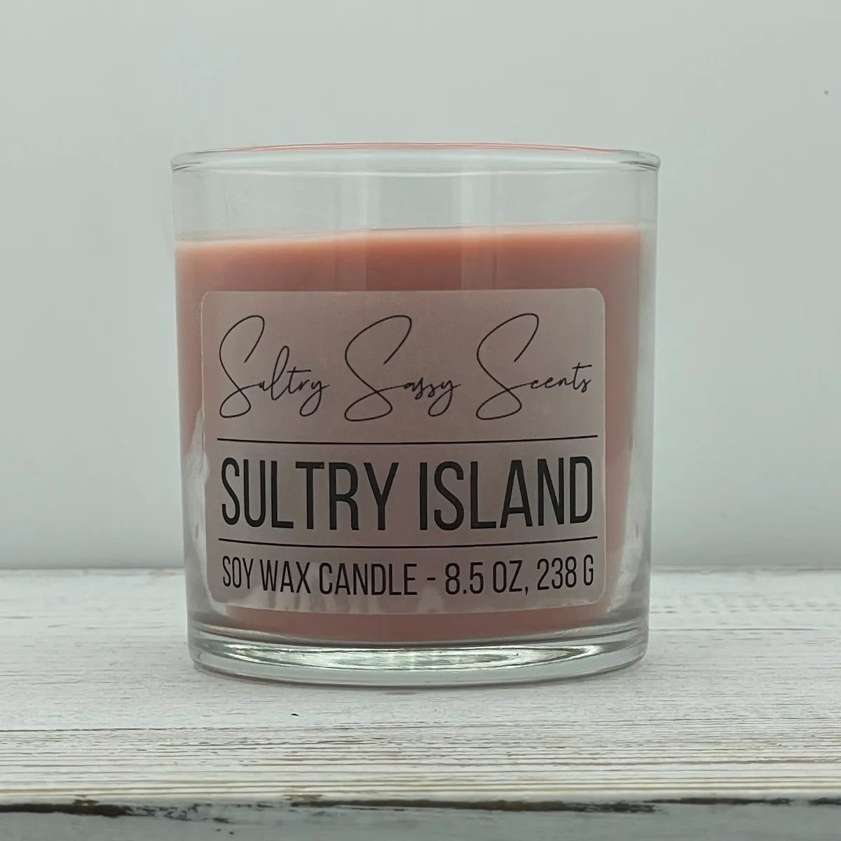 An 8.5-ounce clear glass jar of Sultry Sassy Scents "Sultry Island" soy wax candle featuring a dusty rose pink wax color, centered against a light gray backdrop.