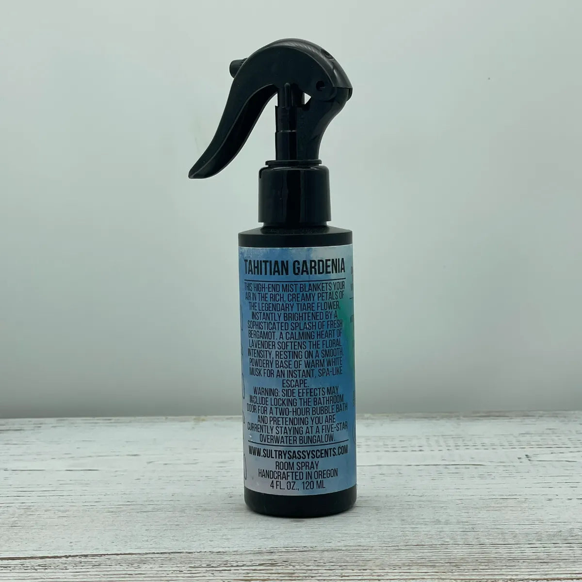Front label of a black spray bottle for Sultry Sassy Scents "Tahitian Gardenia" Room Spray, displaying a crisp text layout describing a high-end spa-like floral escape.