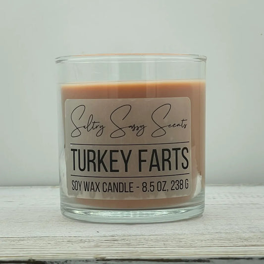 An 8.5-ounce clear glass jar of Sultry Sassy Scents "Turkey Farts" soy wax candle showcasing a light terracotta orange wax color, resting on a white wooden surface.