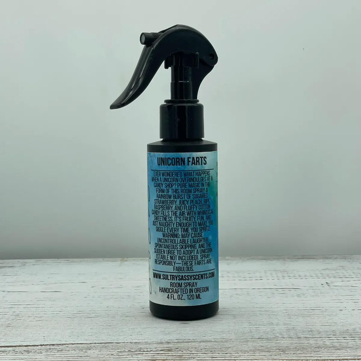 Front label of a black spray bottle for Sultry Sassy Scents "Unicorn Farts" Room Spray, highlighting a fun, whimsical text design describing a sugared strawberry and cotton candy scent.