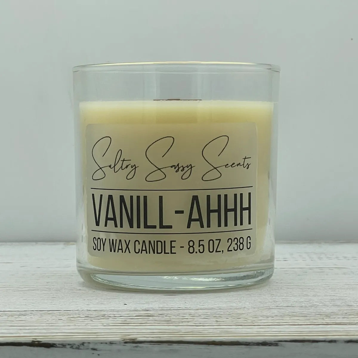 An 8.5-ounce clear glass jar of Sultry Sassy Scents "Vanill-Ahhh" soy wax candle featuring a smooth, creamy off-white wax color and a flat wooden wick.