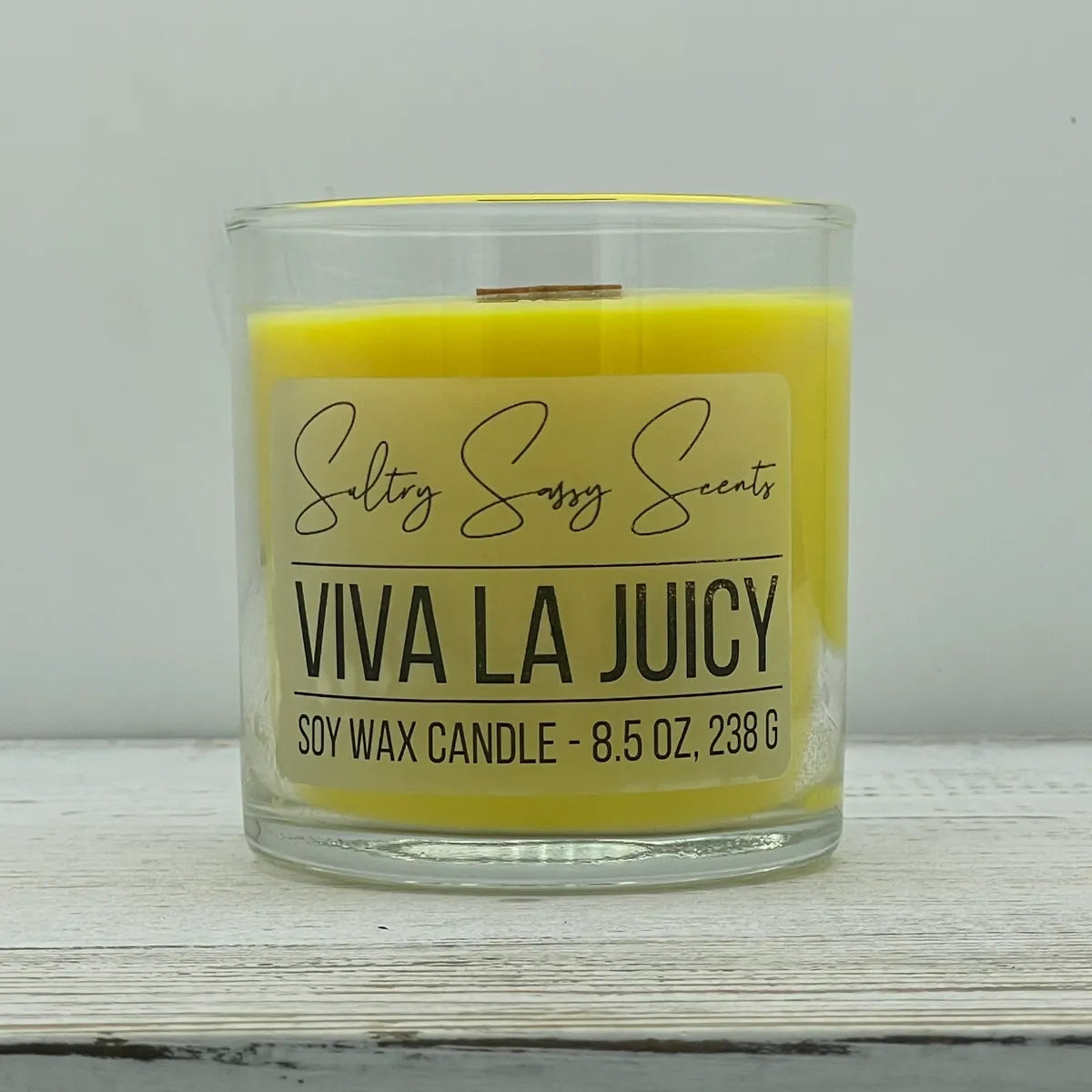 An 8.5-ounce clear glass jar of Sultry Sassy Scents "Viva La Juicy" soy wax candle highlighting a bright, vibrant yellow wax color with a flat wooden wick.