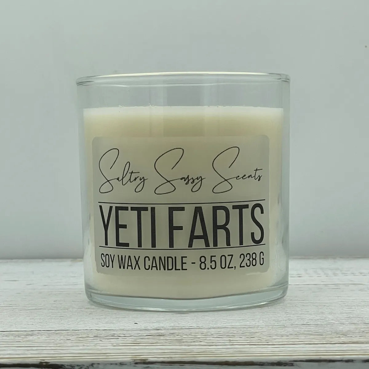 An 8.5-ounce clear glass jar of Sultry Sassy Scents "Yeti Farts" soy wax candle featuring a clean, solid white wax color, centered on a light wood surface.