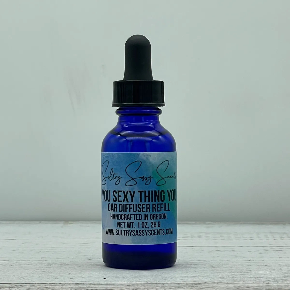 Front label view of a cobalt blue glass dropper bottle containing Sultry Sassy Scents "You Sexy Thing You" Car Diffuser Refill, displaying the central brand logo script.