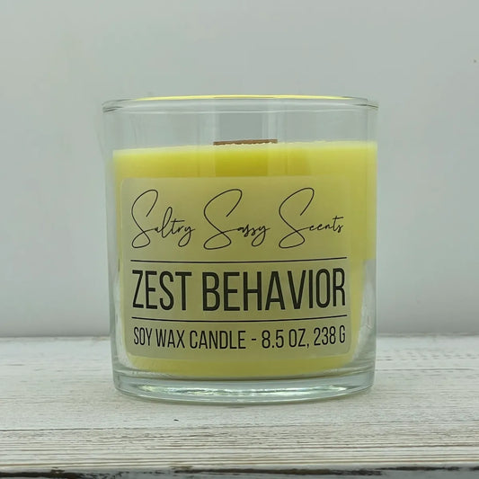 An 8.5-ounce clear glass jar of Sultry Sassy Scents "Zest Behavior" soy wax candle featuring a smooth, vibrant yellow wax color and a flat wooden wick.