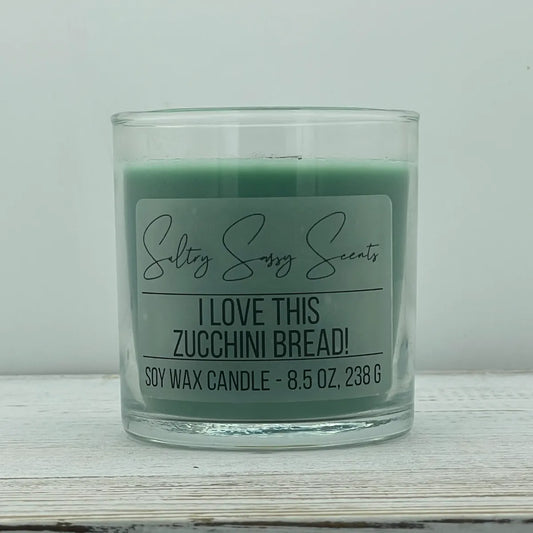 An 8.5-ounce clear glass jar of Sultry Sassy Scents "I Love This Zucchini Bread!" soy wax candle showcasing a muted sage green wax color, centered against a light gray background.